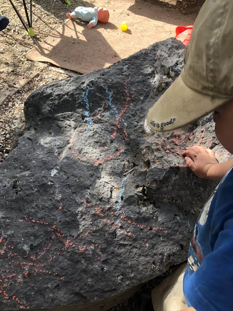 make a fun camping game for your toddler by giving them chalk and asking them to only color certain things (bumpy rocks, pine trees etc)