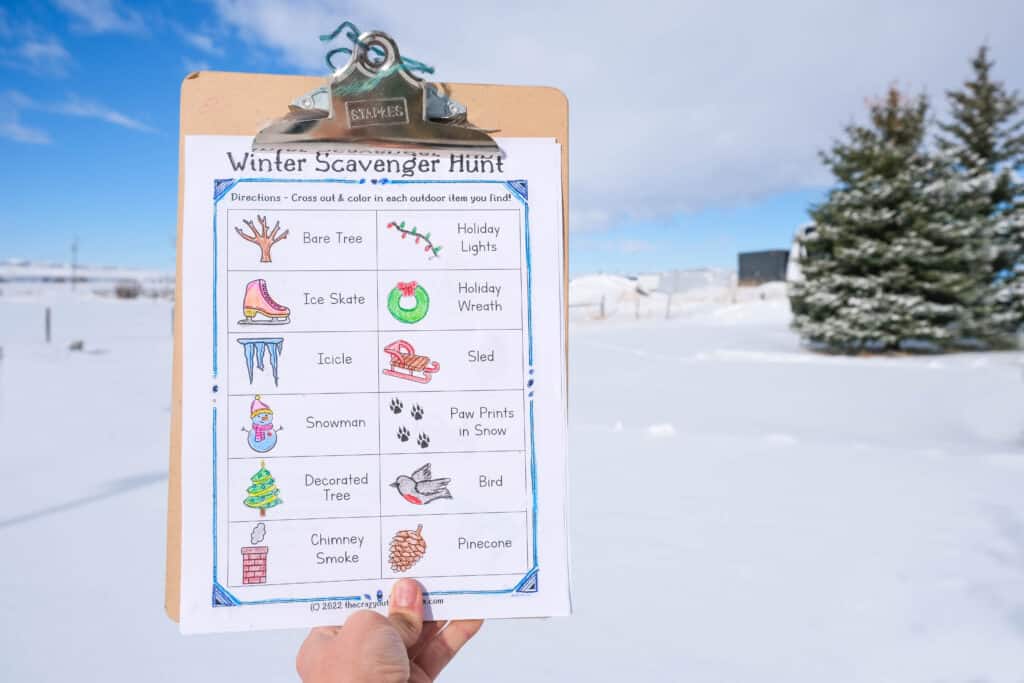 winter scavenger hunt for kids on cliplboard in front of pine tree and snow with winter themed pictures