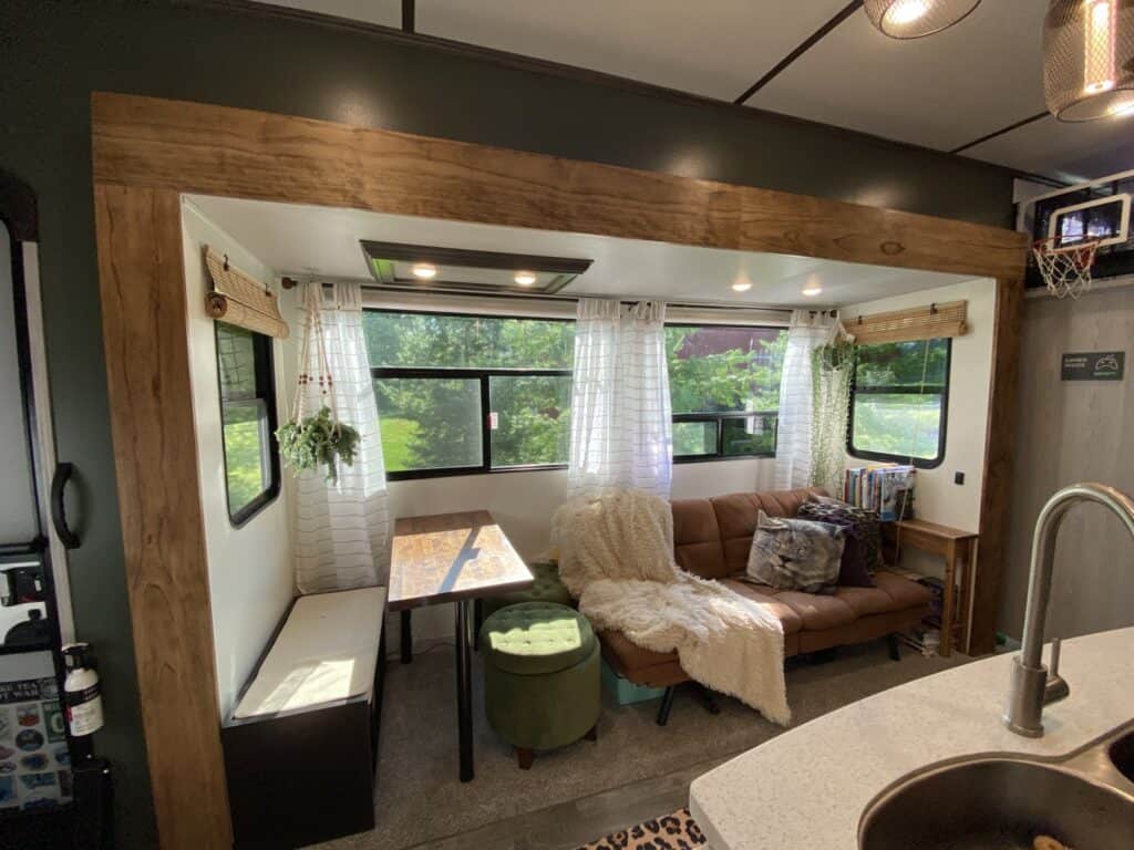 stylish camper interior with wood beams, white curtains, plant and brown couch