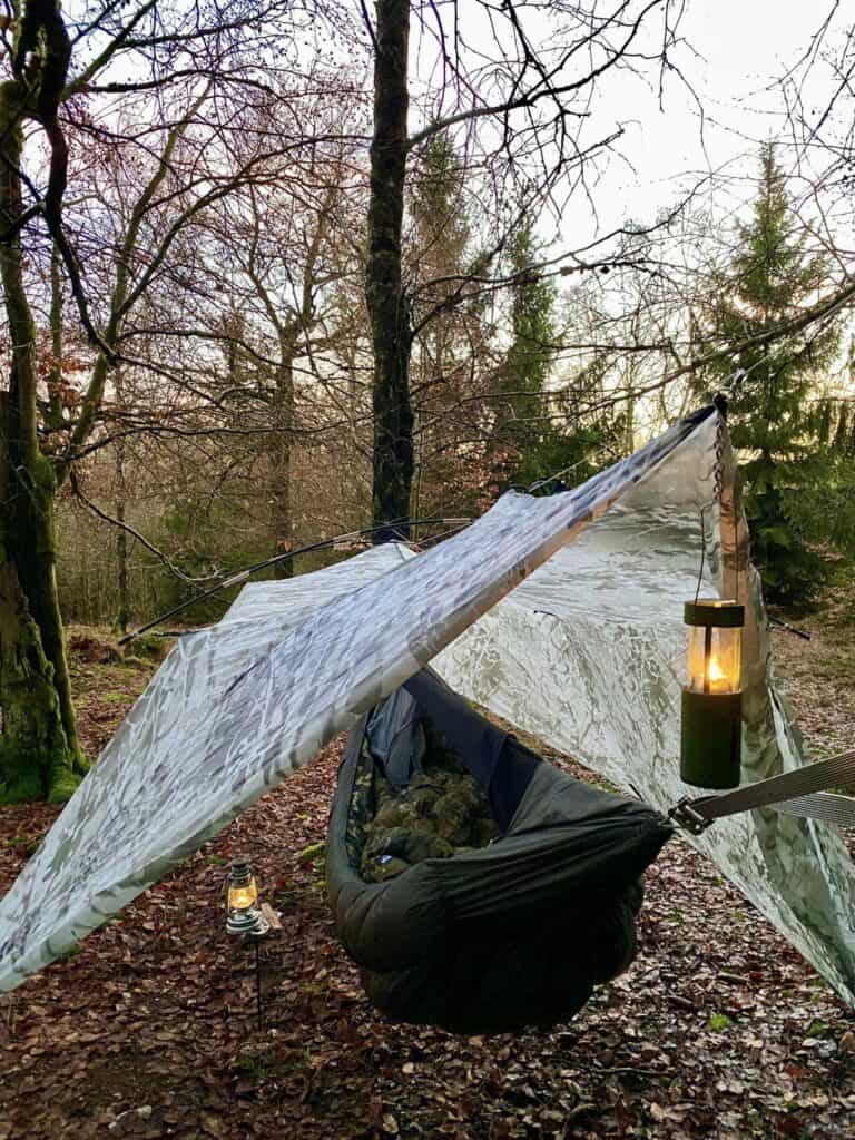 hammock set up in forest with rain fly and lantern