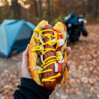 grilled hotdog held in front of tent campsite
