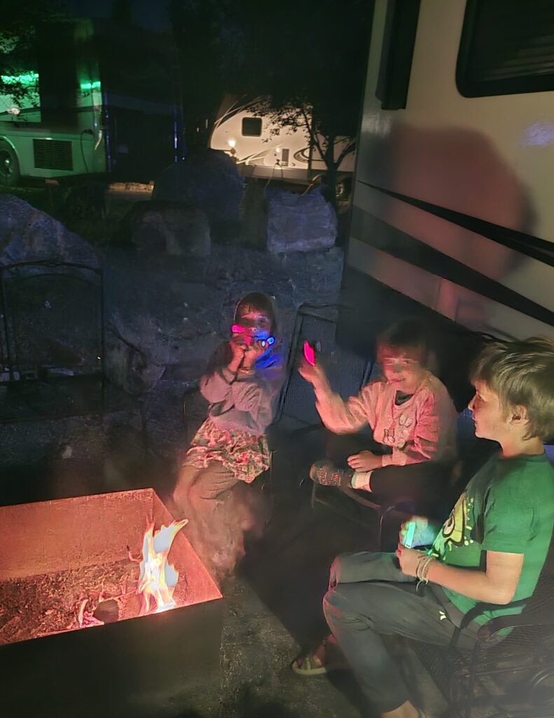 KIDS PLAYING TRIVIA GAME AROUND A CAMPFIRE AT NIGHT